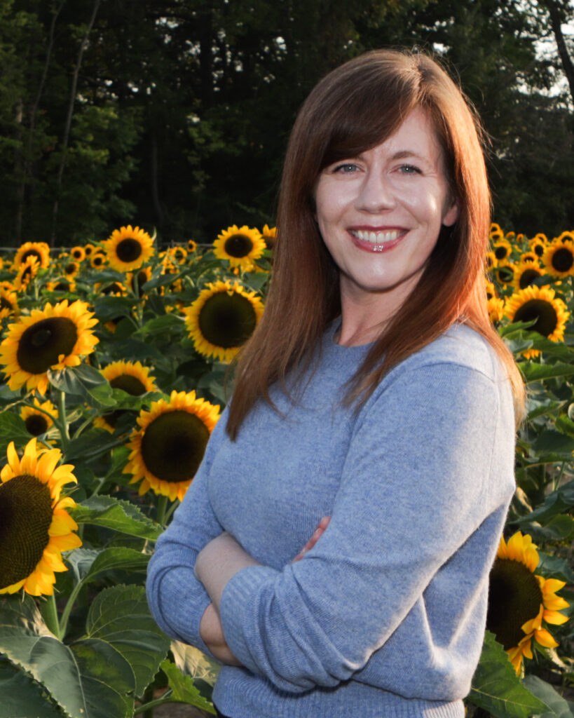 Lisa standing with arms crossed in a field of sunflowers